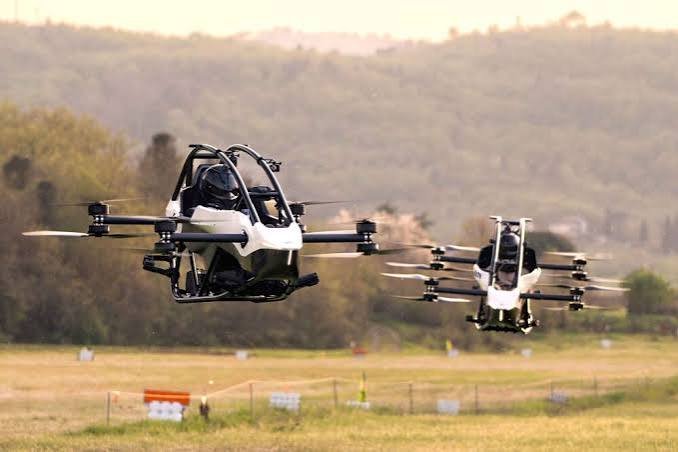 Two open-cockpit personal electric aircraft flying above a field